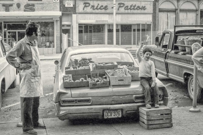boy and his dad selling fruit and vegetables on trunk of pontiac car
